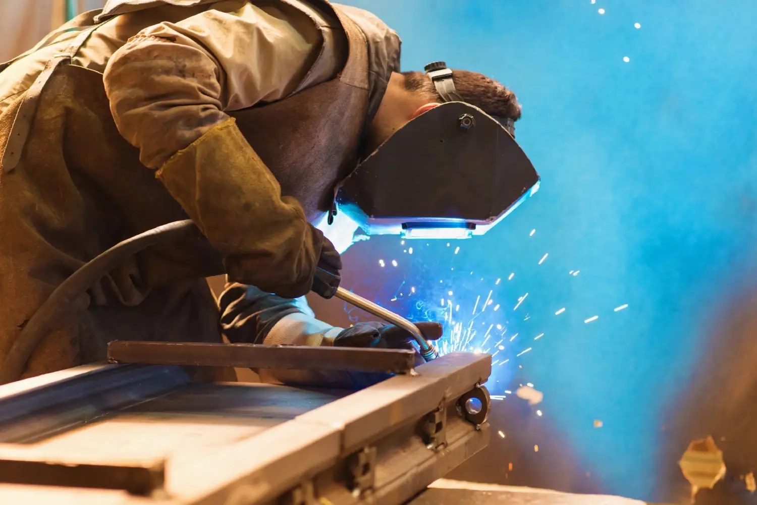 A man welding metal with blue light shining on him.